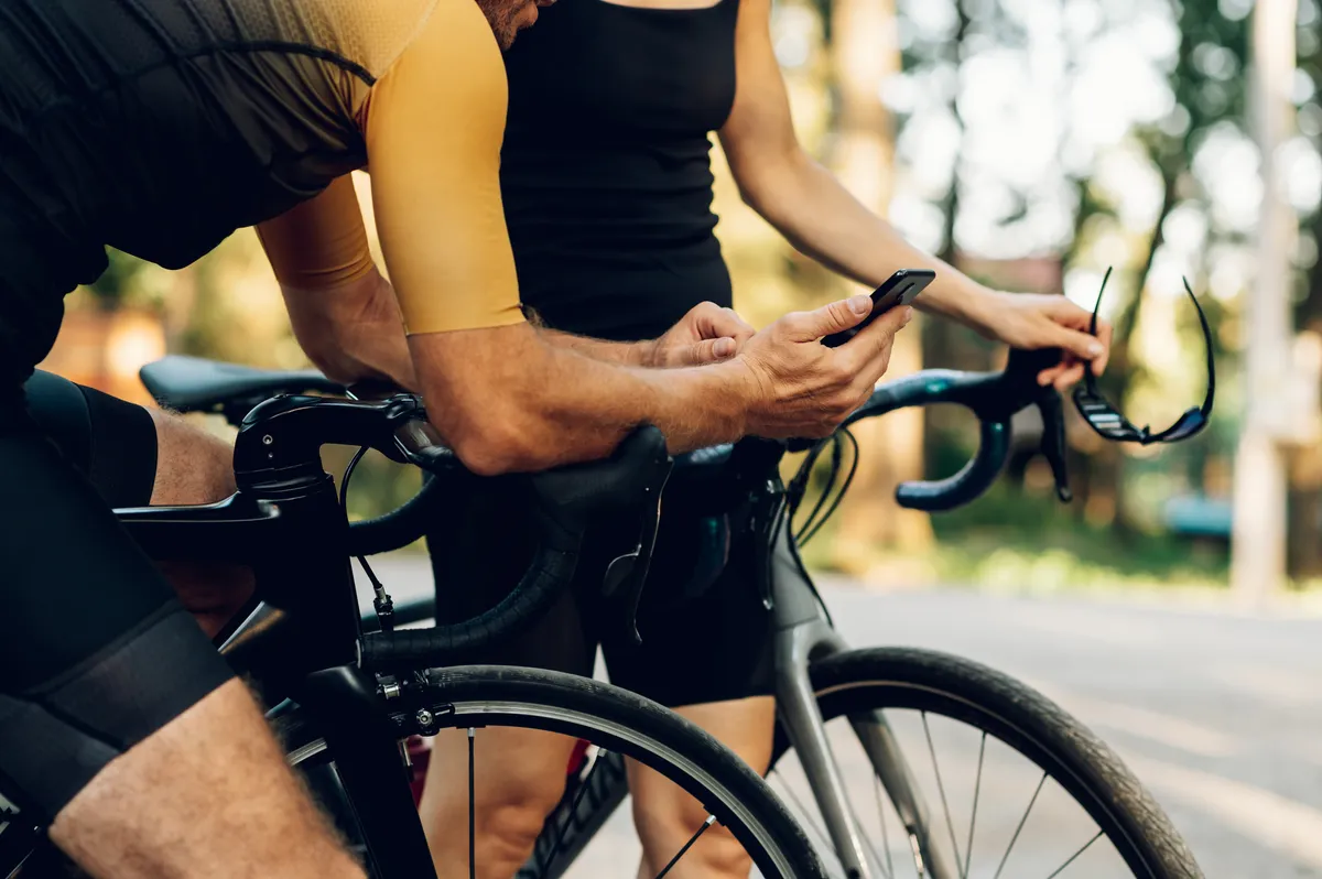 Cropped shot of a cycling woman and man relaxing while standing near their bikes and using a smartphone. Outdoor sport activity. Young smiling couple cycling. Healthy lifestyle.