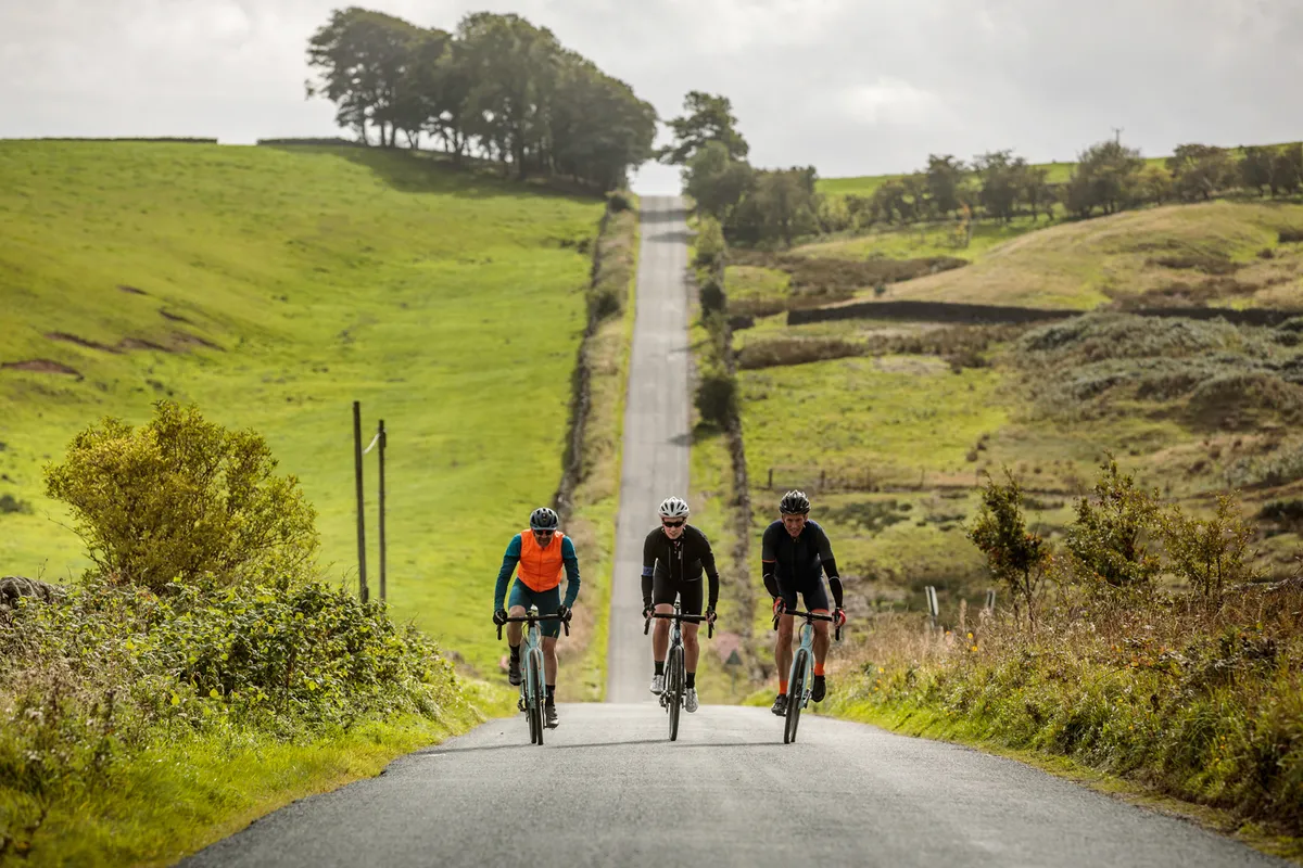Group of three road cyclists riding up a hill on a country lane