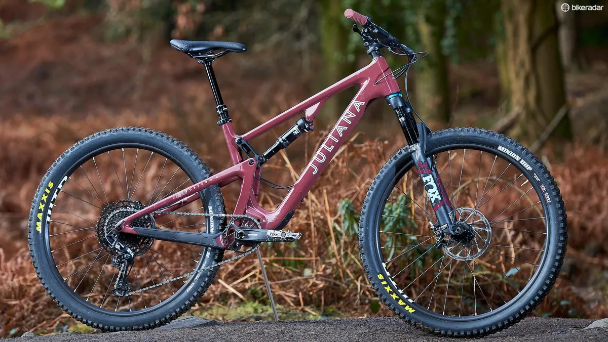 A side-on photograph of the dark red Juliana Furtado mountain bike standing in a forest