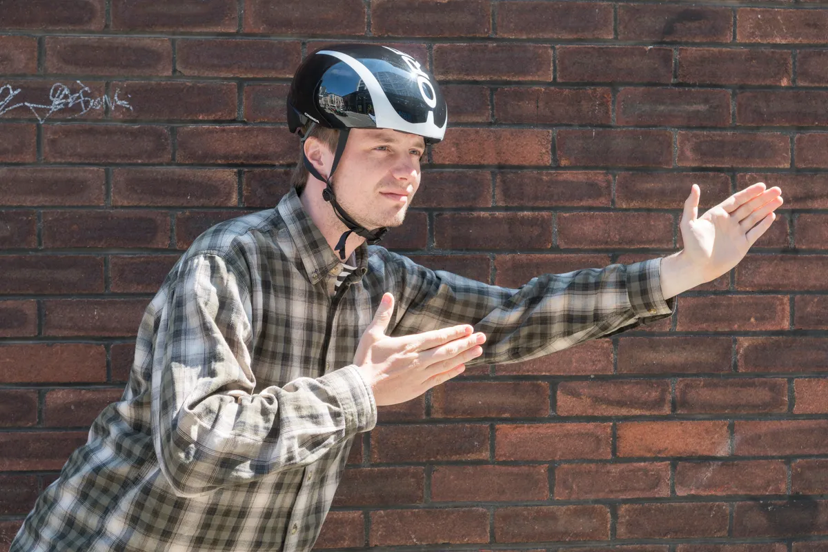 Young man in plaid shirt with arms extended, wearing aero road bike helmet