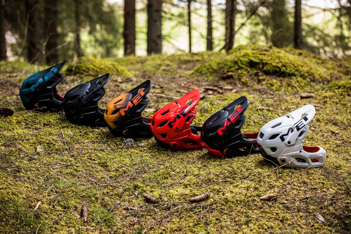 A selection of different colours of the MET Parachute MCR helmet laid out in woodland