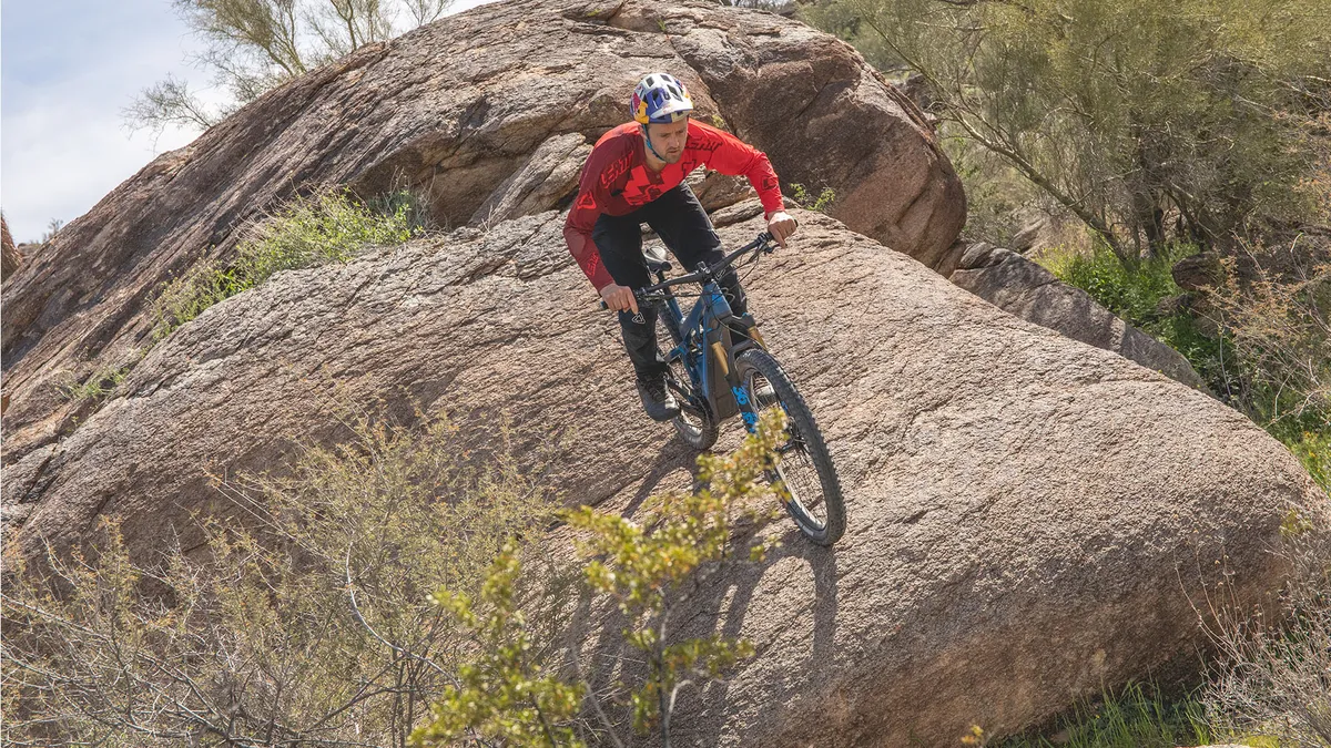 Man rides Pivot electric mountain bike riding down a large rock