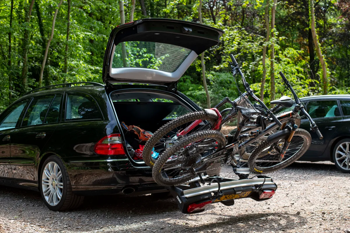 Thule VeloSpace XT3 tow bar mounted bike rack attached to a black car with two bicycles loaded tilted away from the car's open boot