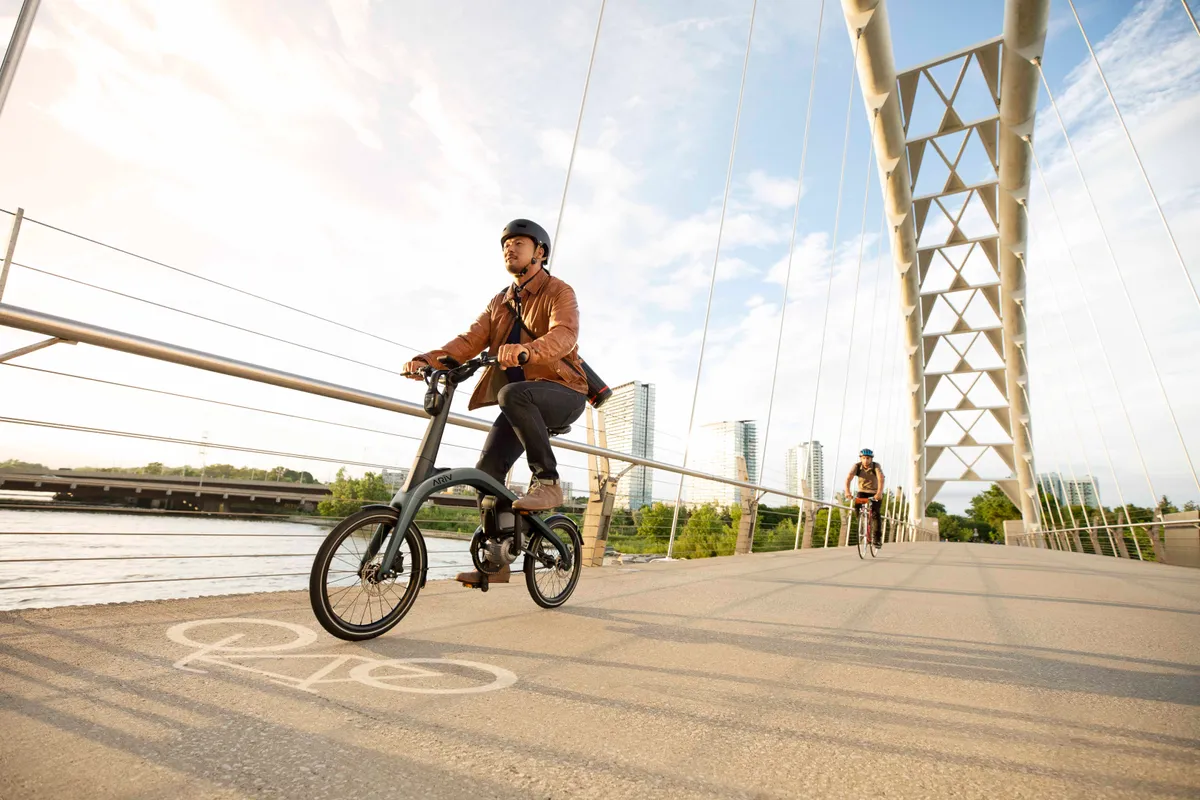 Ariv Merge folding electric bike being ridden over a bridge in the sunshine