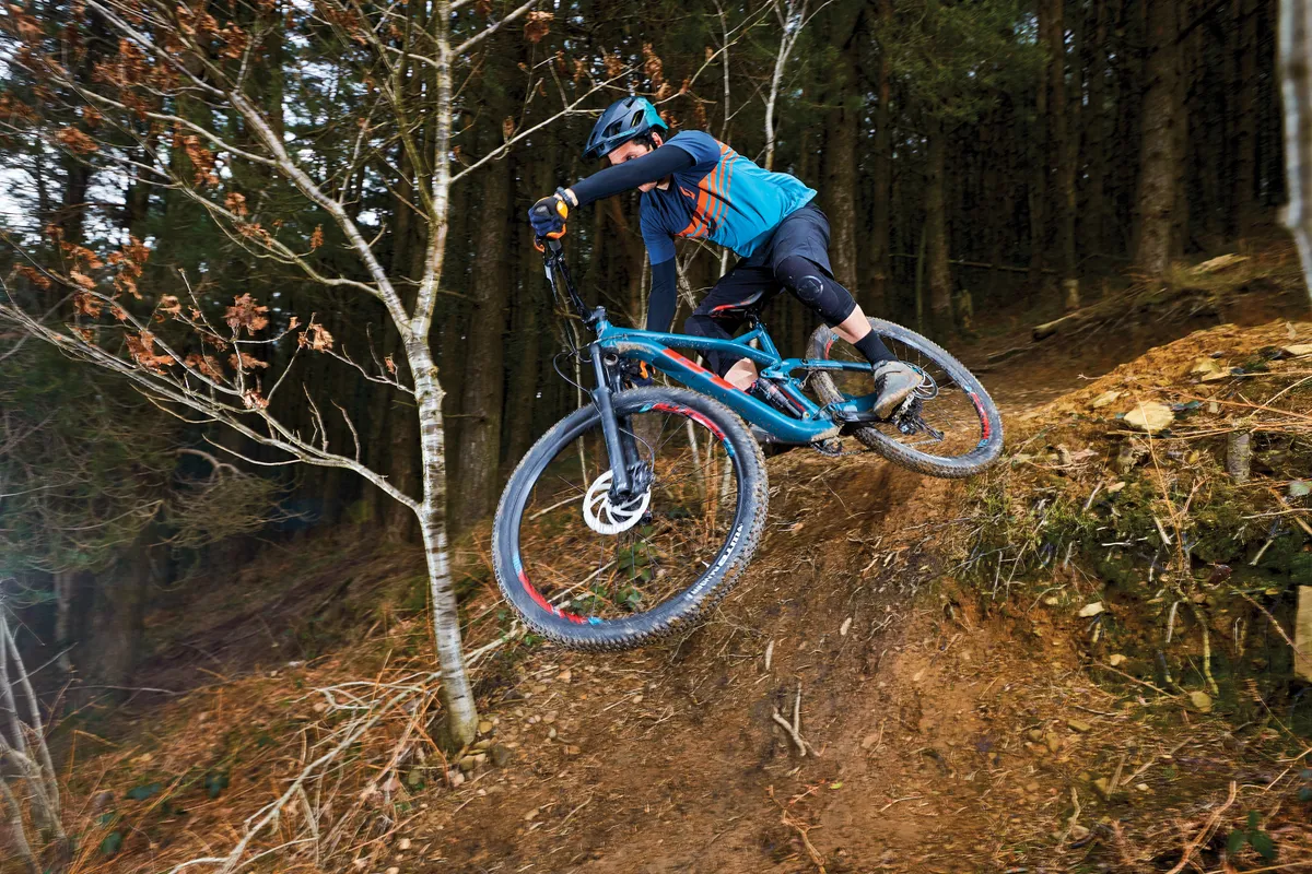Male cyclist riding blue full-suspension mountain bike in woods