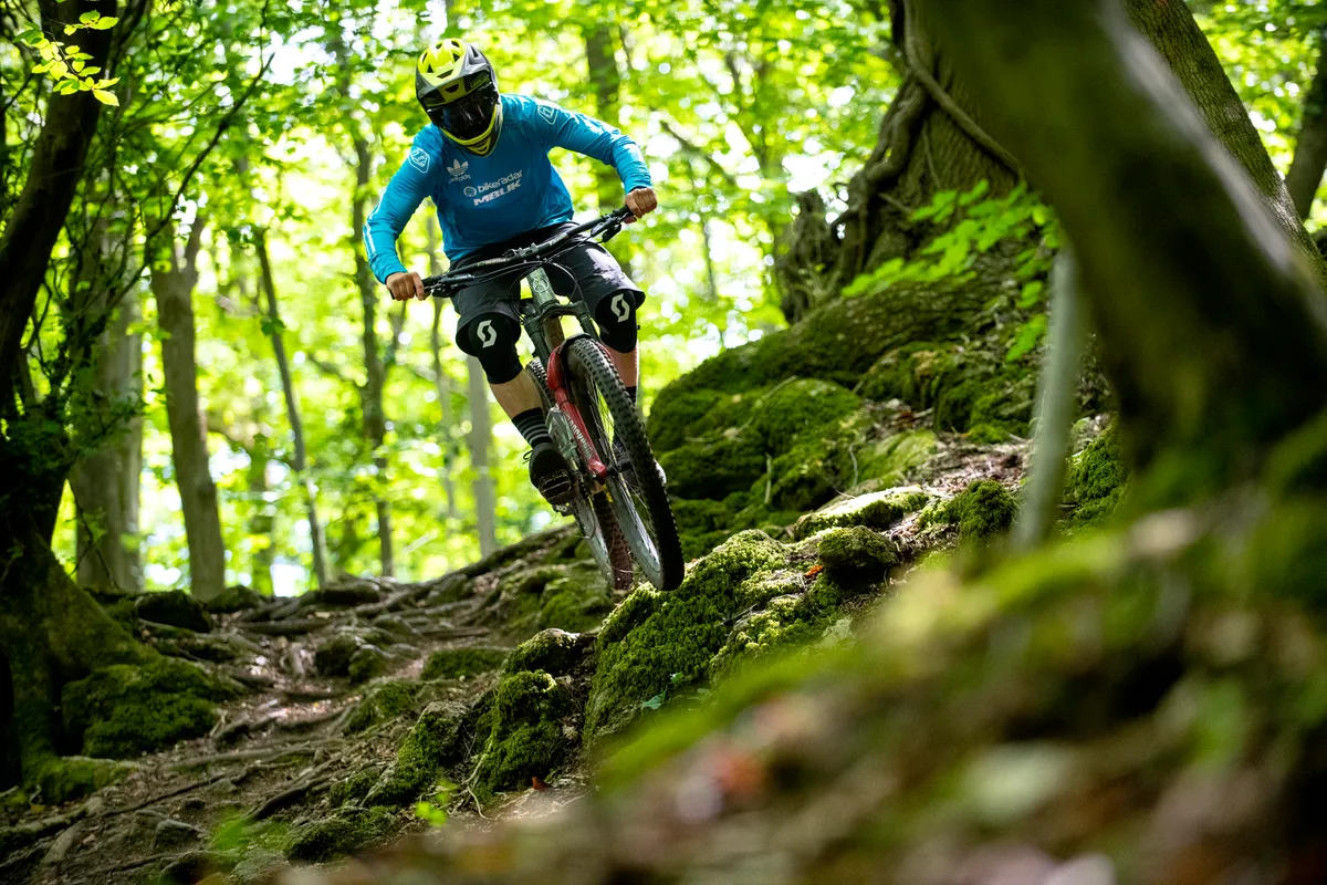 BikeRadar Technical Editor Alex Evans rides his long-term Orange Stage 6 RS enduro mountain bike over some roots in the forest