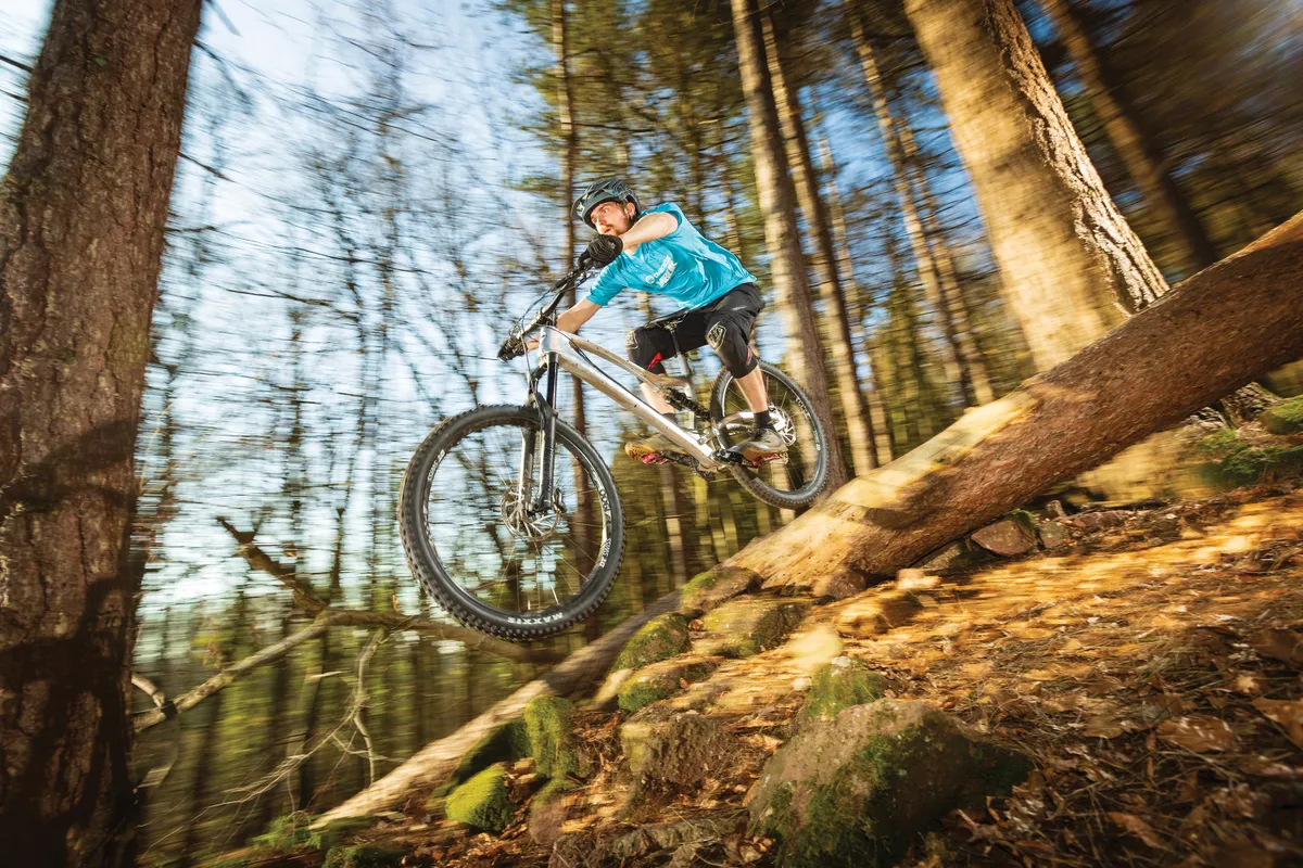 Cyclist riding silver full-suspension bike down hill in woods