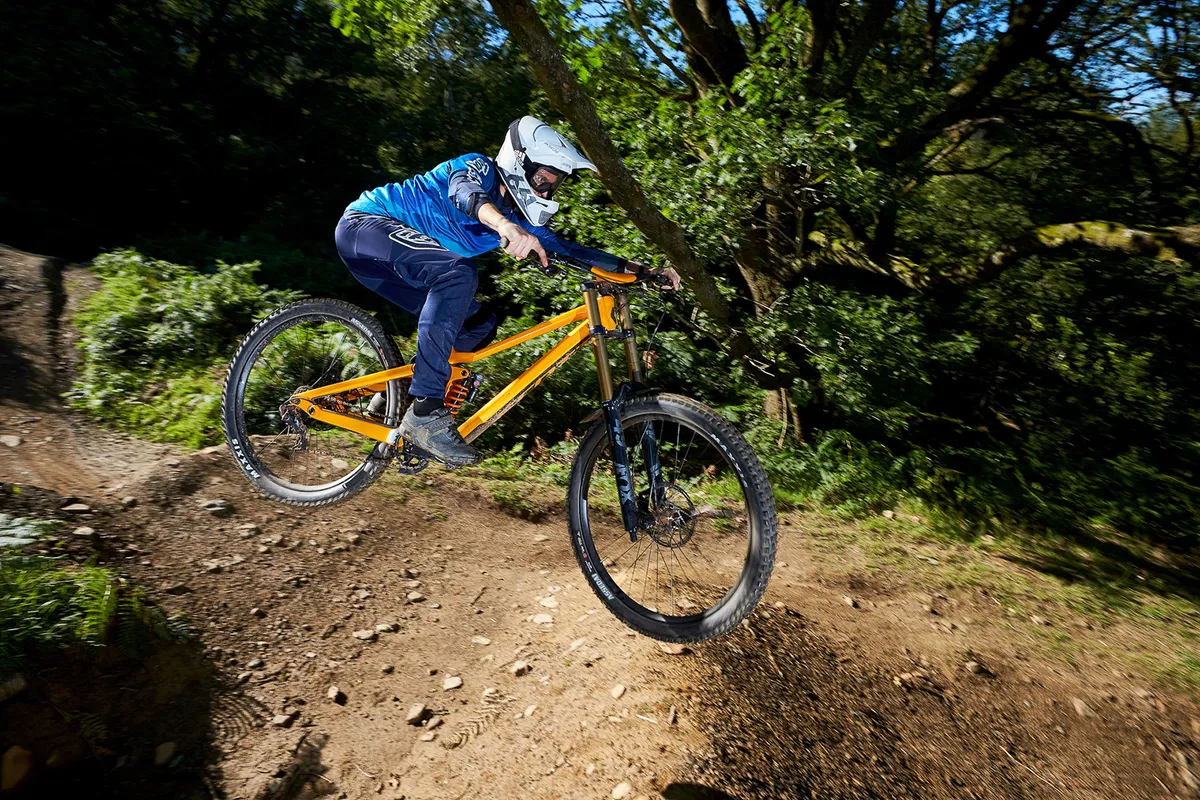 male cyclist riding orange full suspension mountain bike in woods