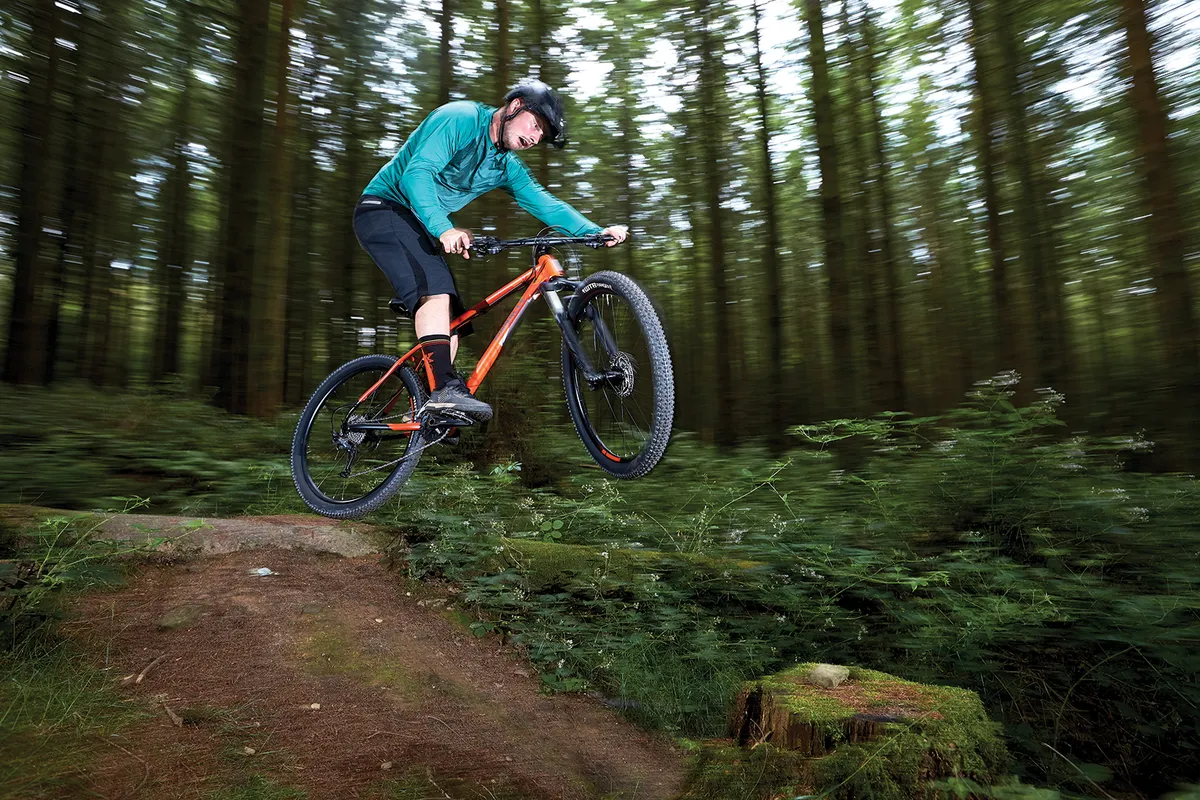 male cyclist riding orange hardtail mountain bike in woods