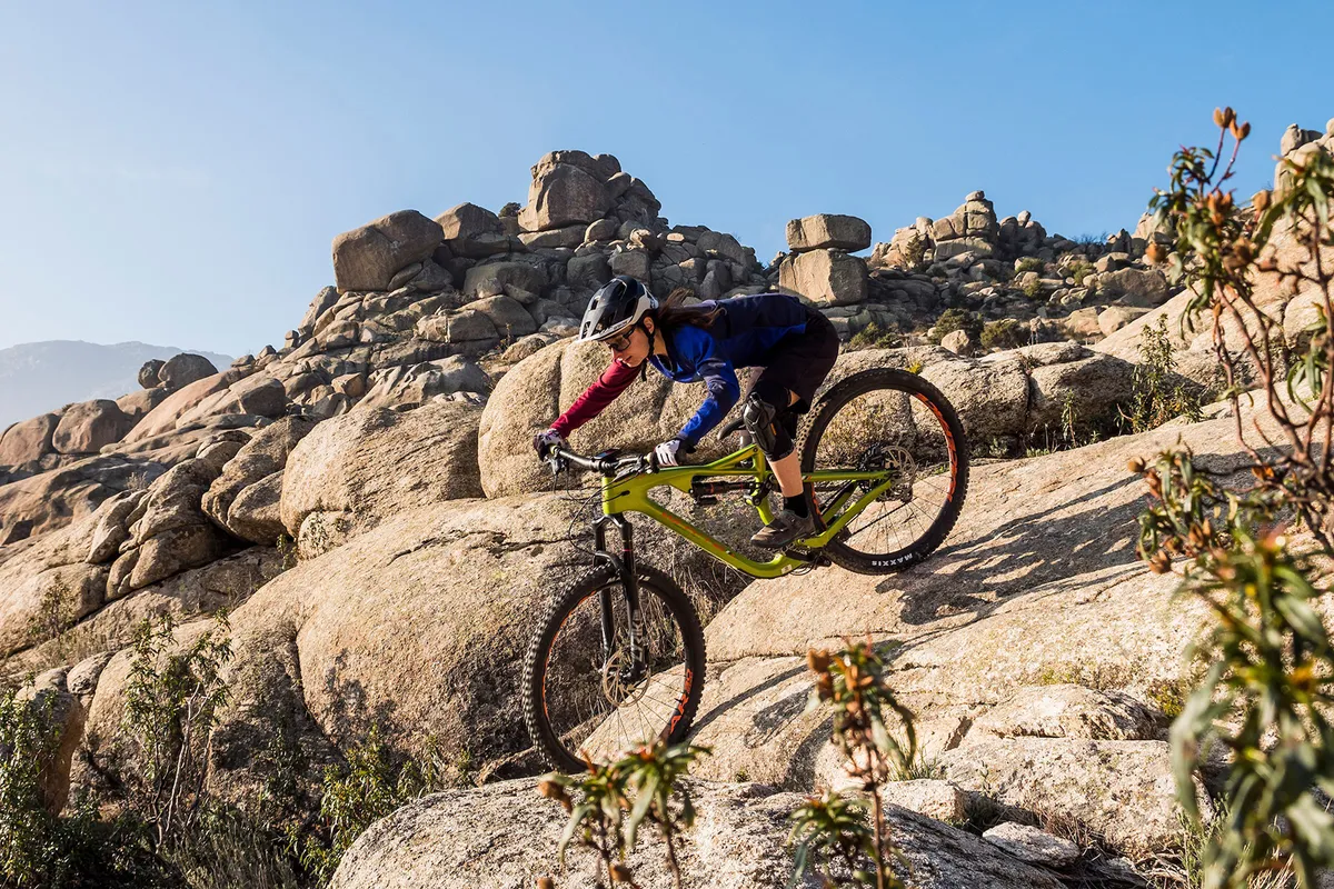 Cyclist in blue top riding a green full suspension mountain bike over rocks