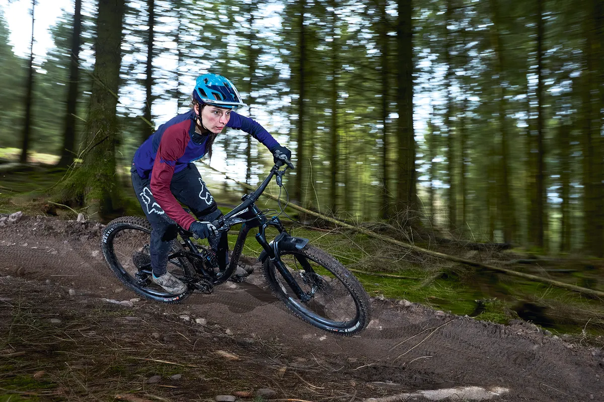 Female cyclist in blue top riding a black full suspension mountain bike