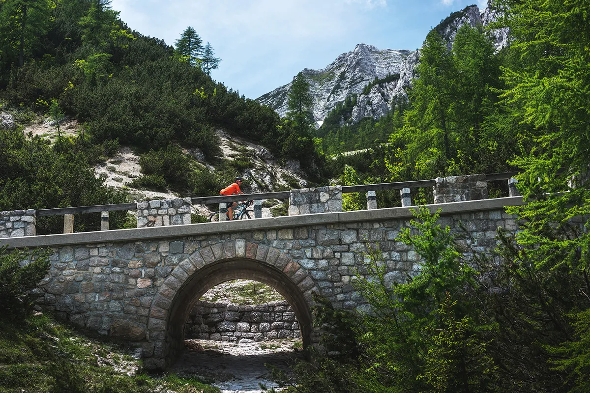 Cyclists riding across a stone bridge in the Julian Alps of Slovenia