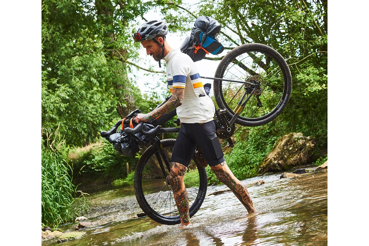 Male cyclist crossing a stream on foot while carrying his touring bike