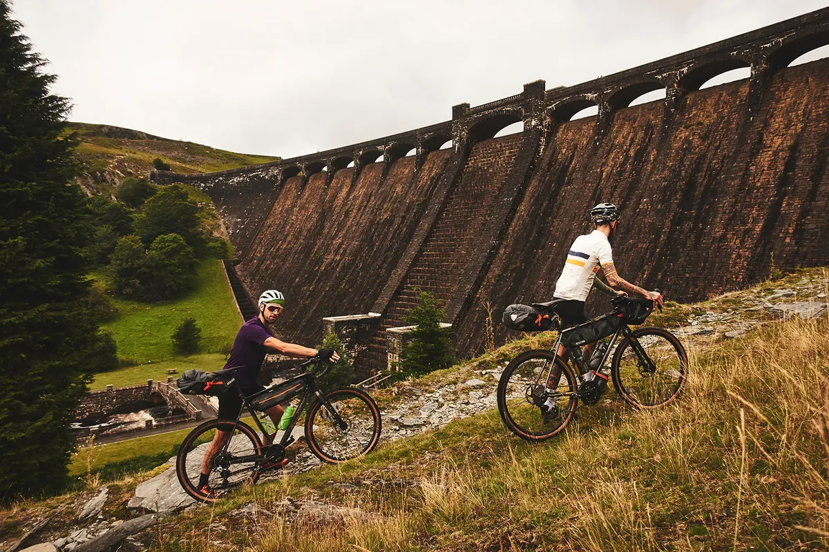 Two male cyclists riding gravel bikes next to a dam in Wales