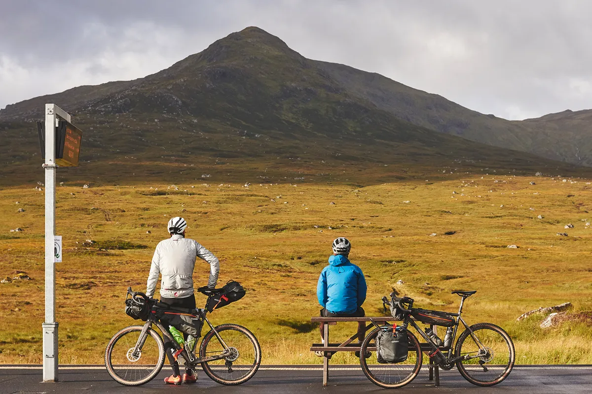 Two cyclists take a break to enjoy the view while bikepacking through the highlands of Scotland