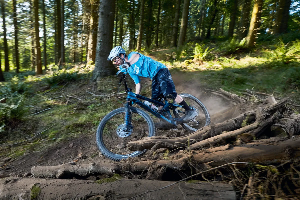 Cyclist riding a Transition Scout GX full-suspension mountain bike through the Forest of Dean