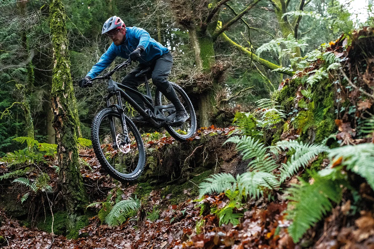 Cyclist in blue top riding the Evil Offering GX Hydra full suspension mountain bike through woodland