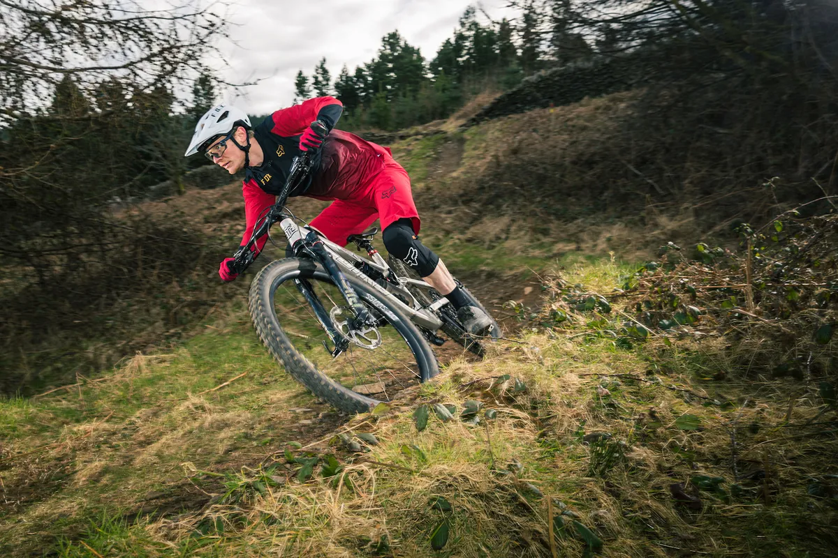 Cyclist in red and black riding the Bird Aether 9 full suspension mountain bike downhill