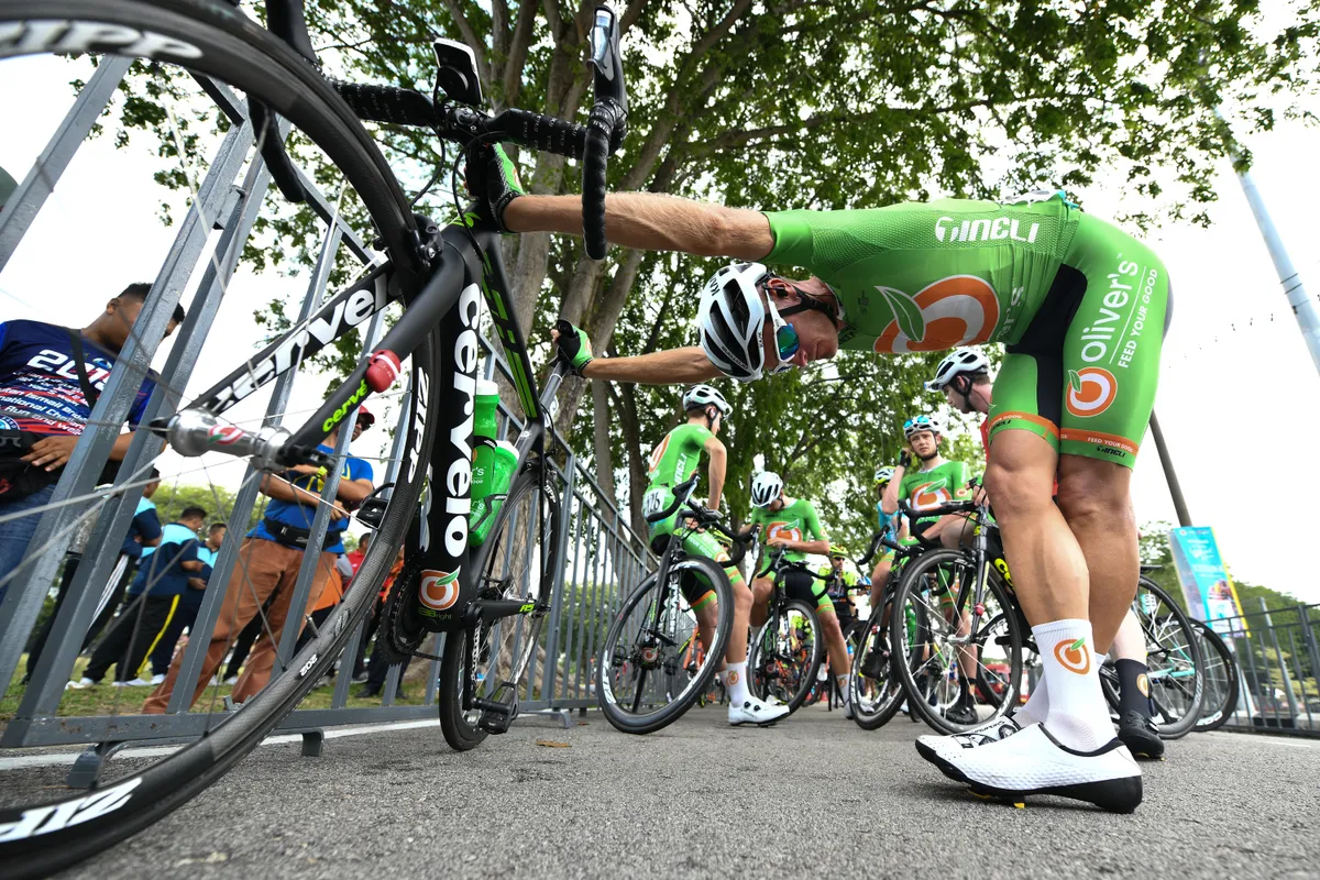 Professional cyclist stretching legs on side of road.