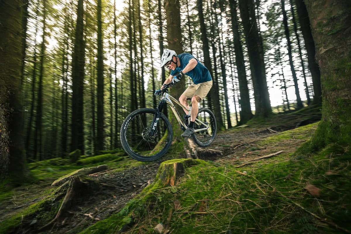 Male cyclist in blue top riding the Lapierre Zesty AM 6.9 CF full suspension mountain bike through woodland