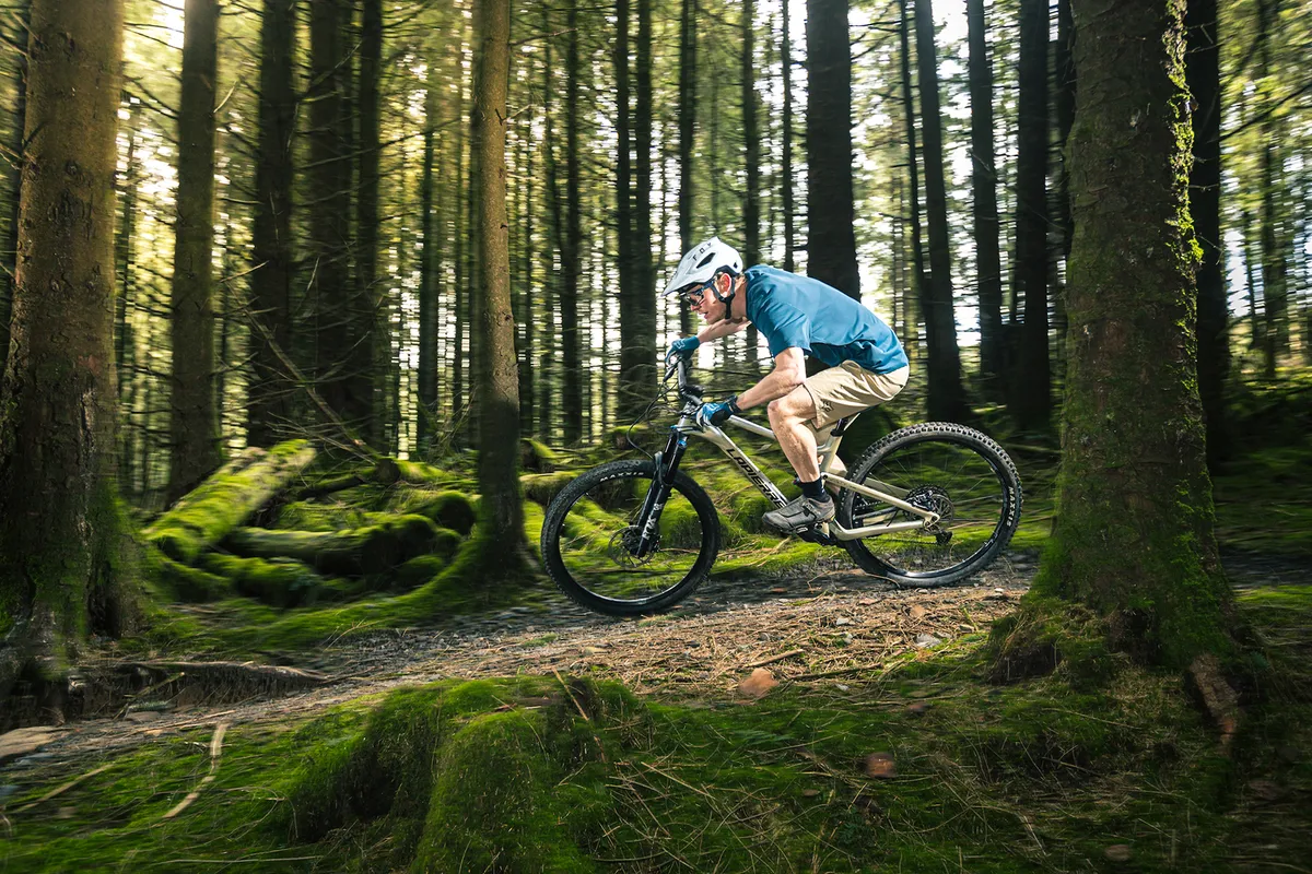 Male cyclist in blue top riding the Lapierre Zesty AM 6.9 CF full suspension mountain bike through woodland