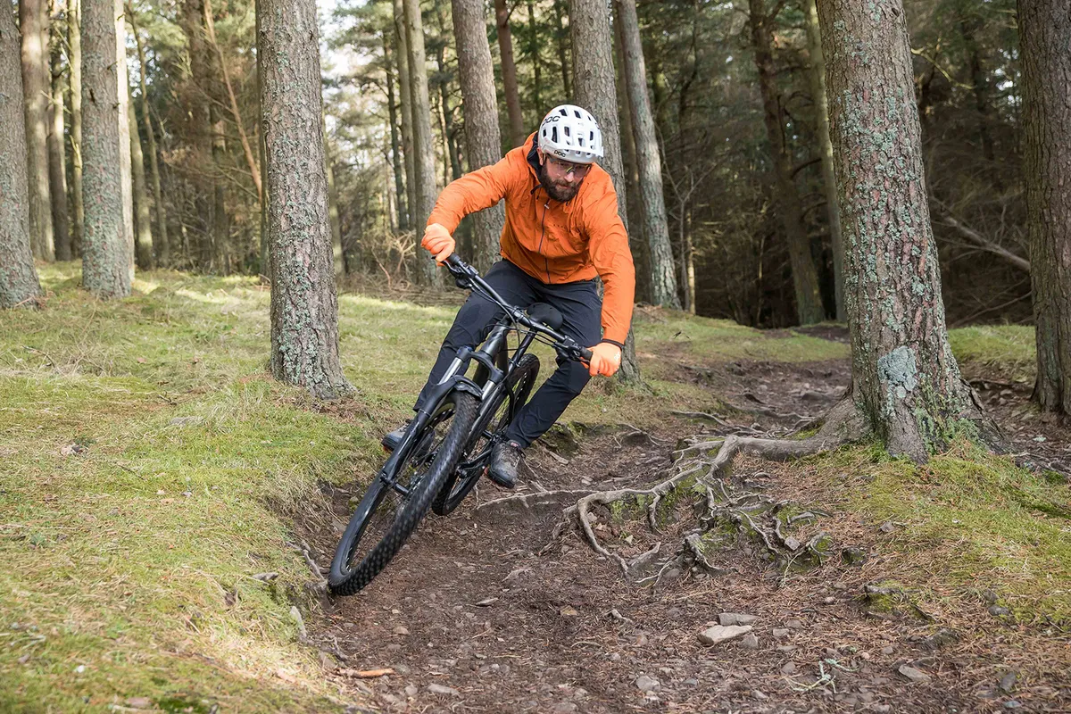 Cyclist in orange top riding the Specialized Rockhopper Comp hardtail mountain bike through woodland