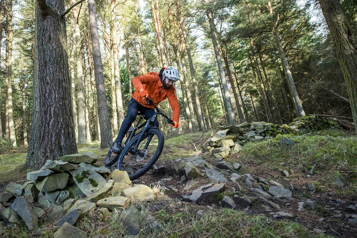 Cyclist in orange top riding the Specialized Rockhopper Comp hardtail mountain bike through woodland