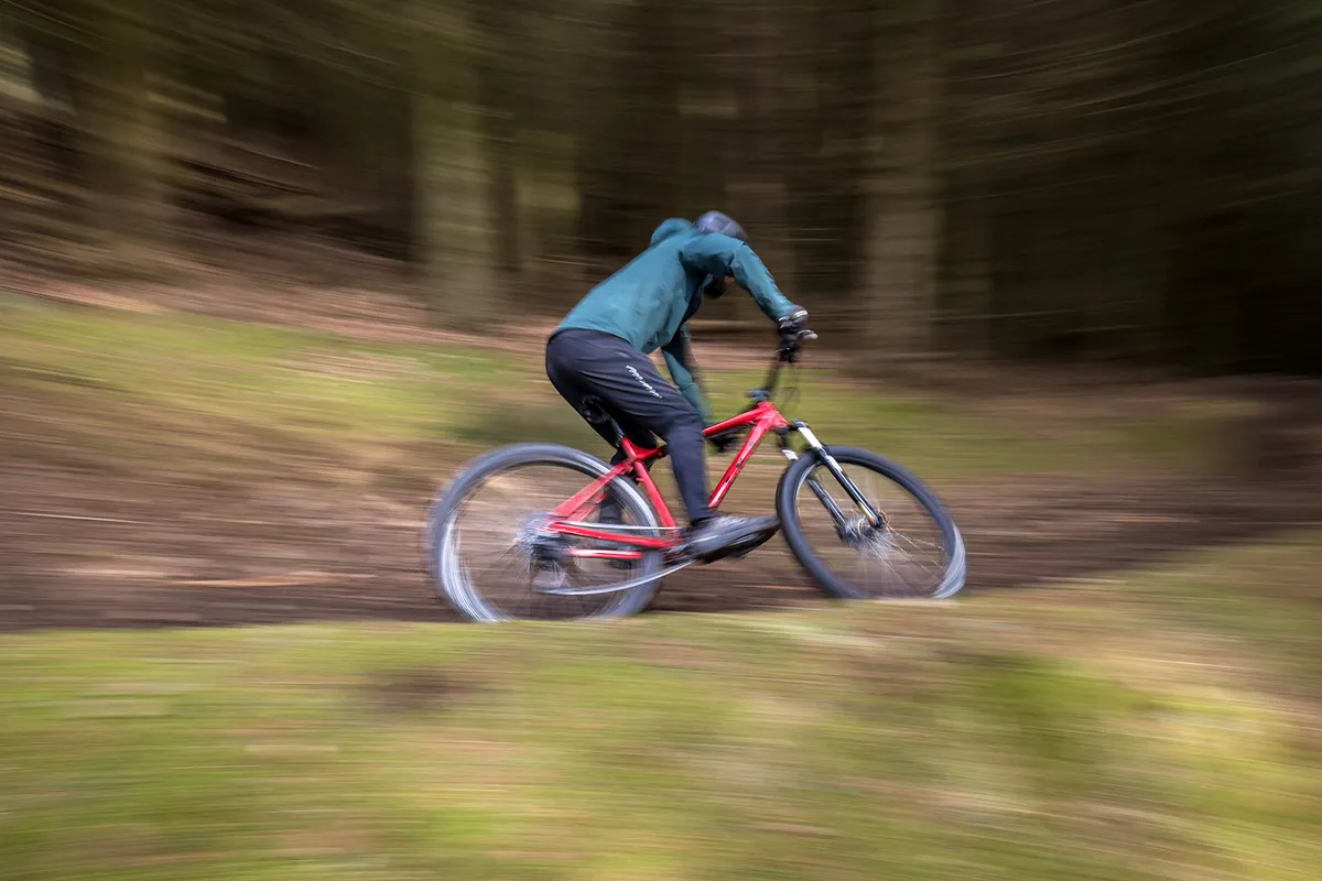 Cyclist in blue top riding the Vitus Nucleus 29 VRS hardtail mountain bike through woodland