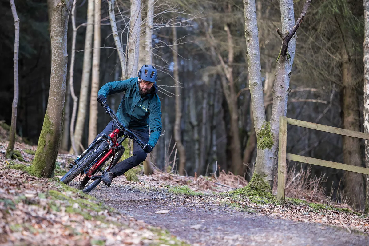 Cyclist in blue top riding the Vitus Nucleus 29 VRS hardtail mountain bike through woodland