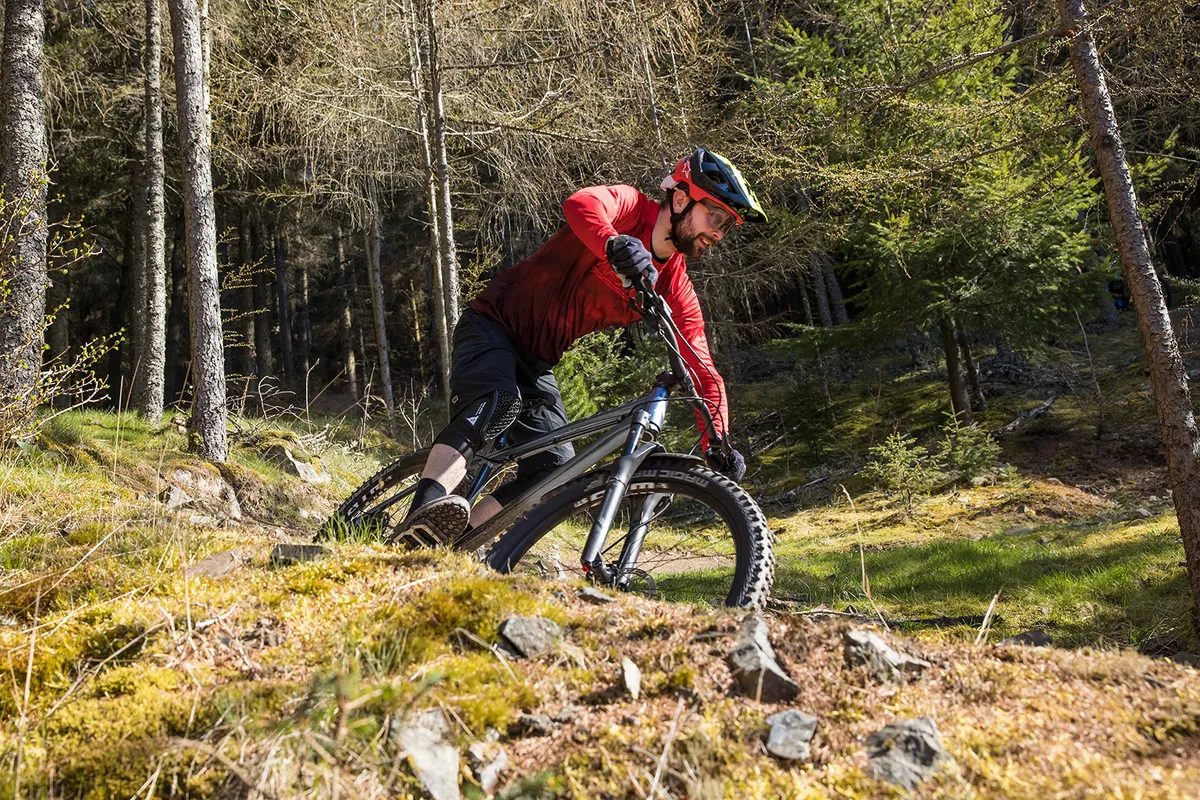 Cyclist in red top riding the Vitus Sentier 27 hardtail mountain bike over rough ground