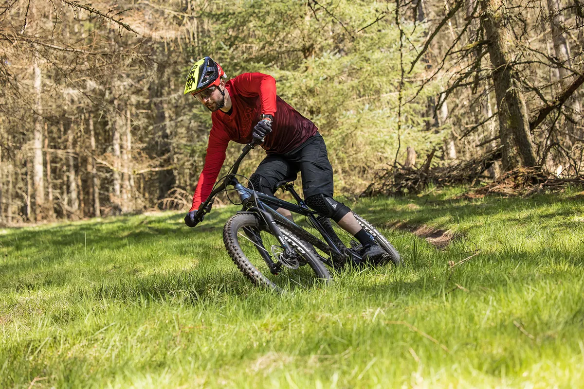 Cyclist in red top riding the Vitus Sentier 27 hardtail mountain bike through woodland