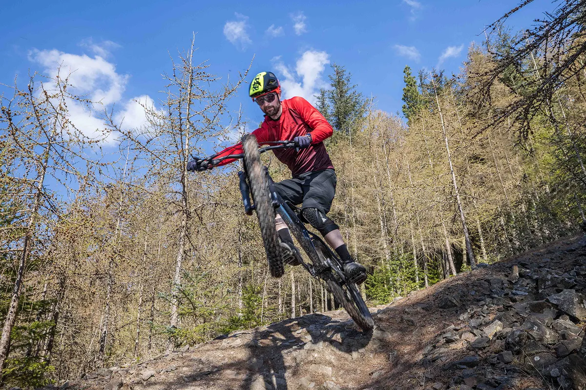 Cyclist in red top riding the Vitus Sentier 27 hardtail mountain bike over rough ground