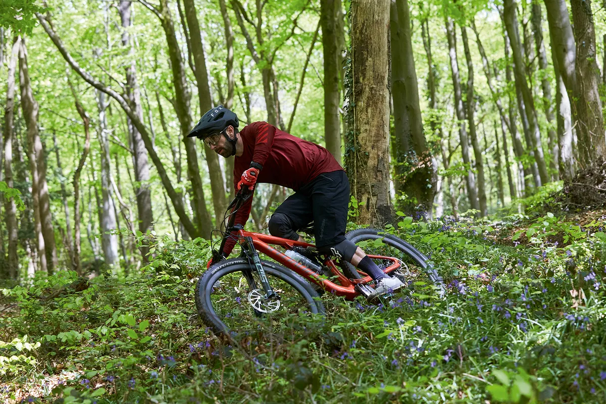 Cyclist in red top riding the Specialized Epic EVO Expert full suspension mountain bike through woodland