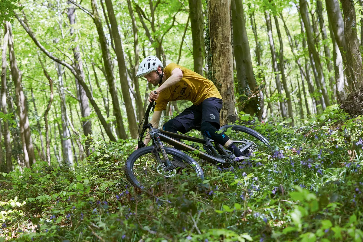 Male cyclist riding the Transition Spur X01 Carbon full suspension mountain bike through woodland
