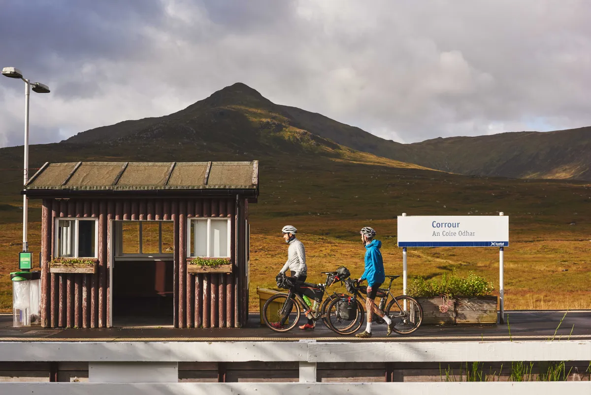 Two cyclists on a train station platform in the Scottish Highlands during a bikepacking trip