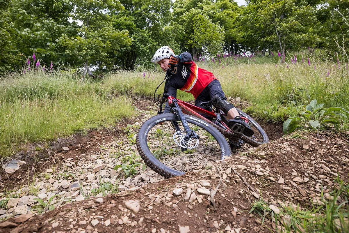 Male cyclist in red riding the Vitus Escarpe 29 CRS trail mountain bike through woodland