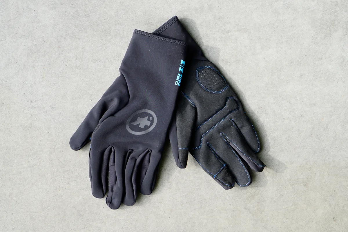 A pair of Assos winter gloves placed over one another, with one showing the top and the other showing palm, photographed against a grey tile background