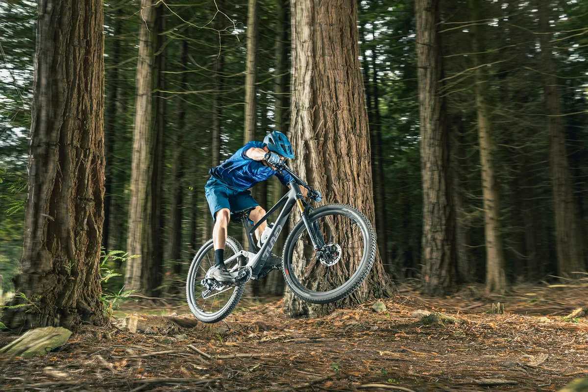 Male cyclist in blue riding the Scott Spark 900 Tuned AXS full suspension mountain bike through woodland