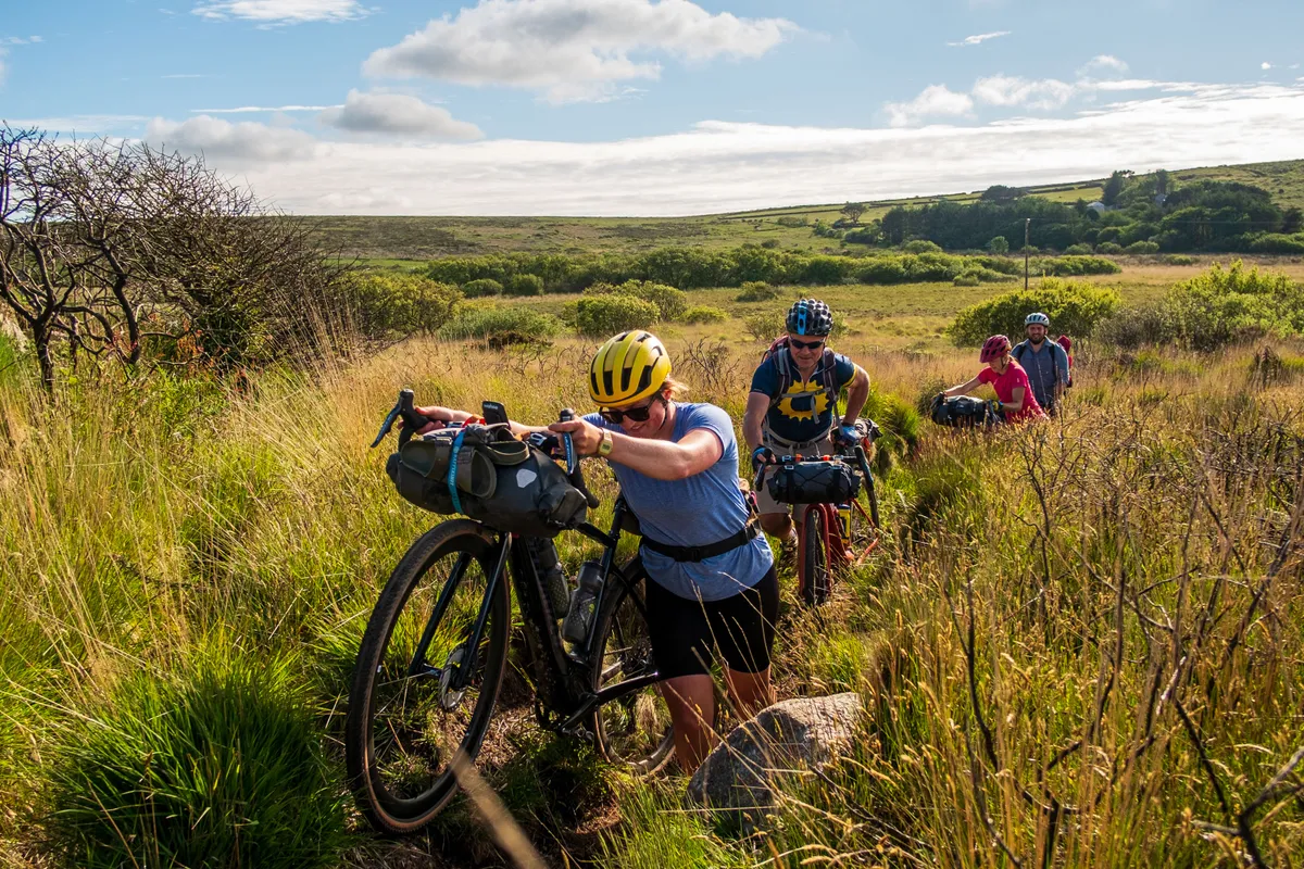 Katherine Moore (Unpaved podcast), Rob Penn (freelance journalist), Sophie Gordon (Cycling UK) and Stefan Amato (Pannier) push their bikes along a difficult overgrown bit of singletrack across the Penwith Moors during a recce ride of Cycling UK's West Kernow Way, June 2021. The 230km route is part of the EU-funded EXPERIENCE project to develop sustainable year-round tourism activities in Cornwall.