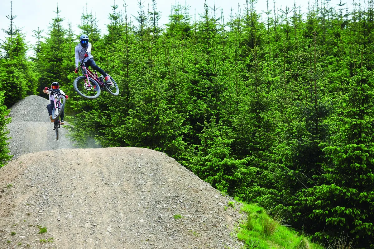 Two cyclists riding downhill bikes on jumps