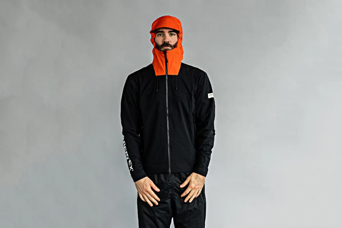 Model wearing Albion Zoa Rain Shell jacket in black and orange