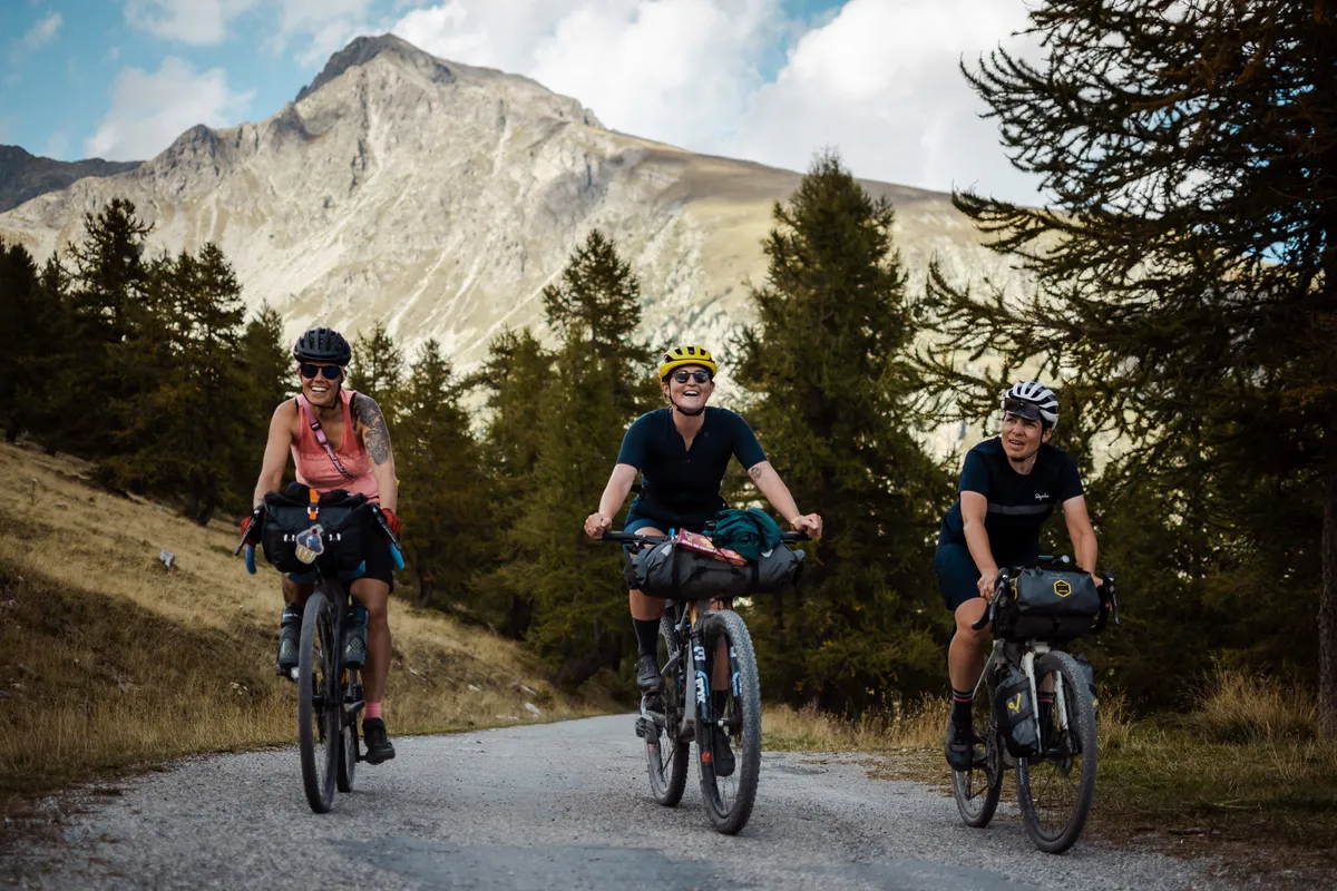 Group of three female cyclists climbing on loaded bikes