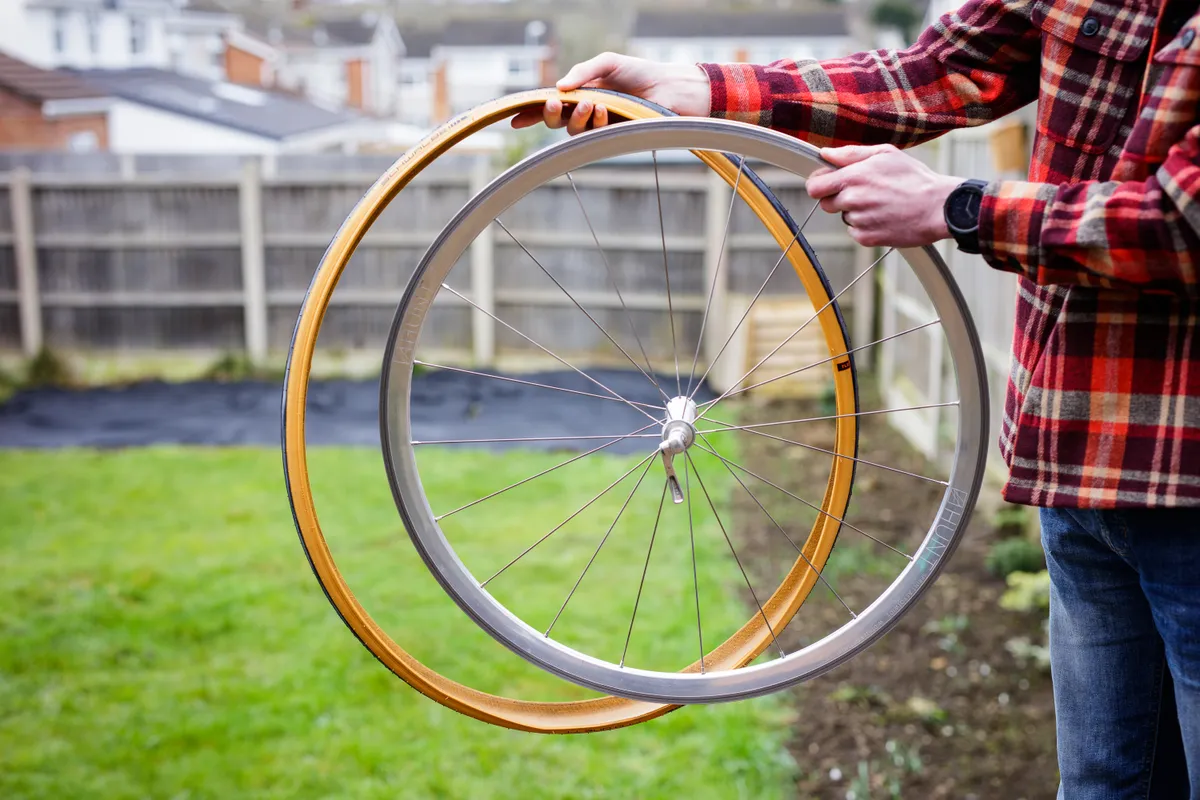 Person holding bicycle tyre next to a wheel