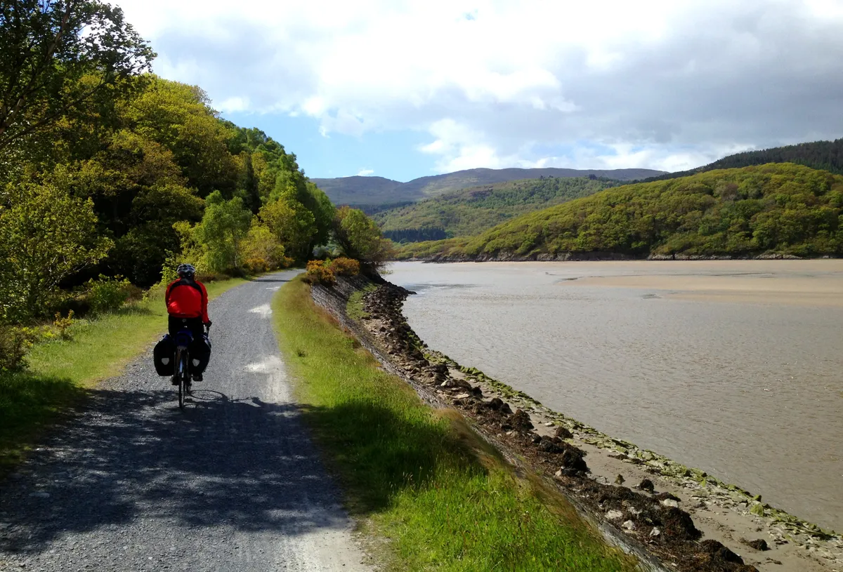 A man cycling along a cycle path next to a river in Wales, Mawddach Trail, National Route 8.