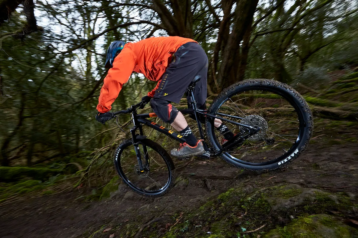 Male cyclist in orange top riding the Voodoo Bizango hardtail trail mountain bike through woodland