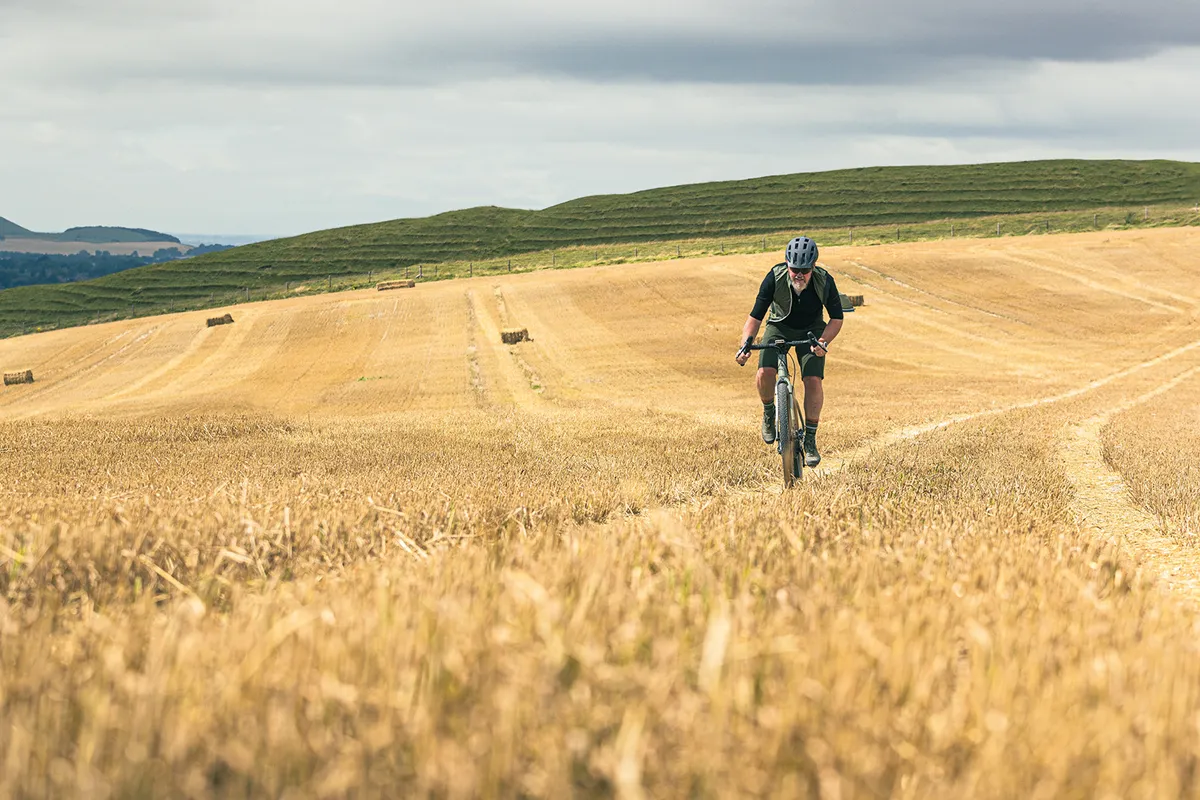 Male cyclist riding the Cairn Brave 1.0 gravel eBike through fields