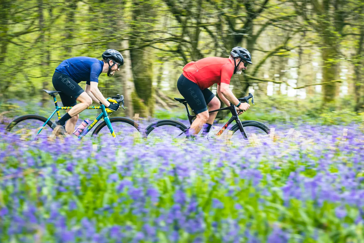 Two male cyclist riding gravel bikes through a bluebell woodland
