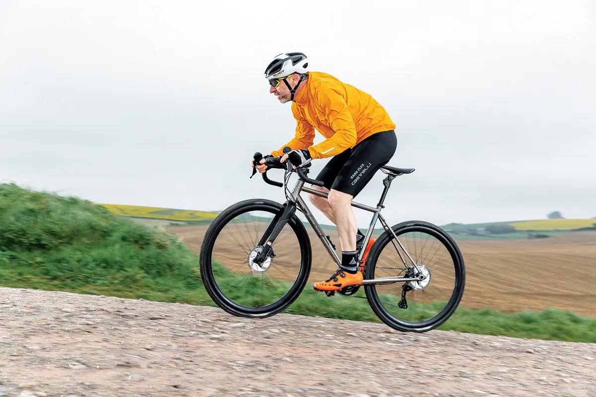Male cyclist in orange top riding the All-City Cosmic Stallion Ti gravel bike