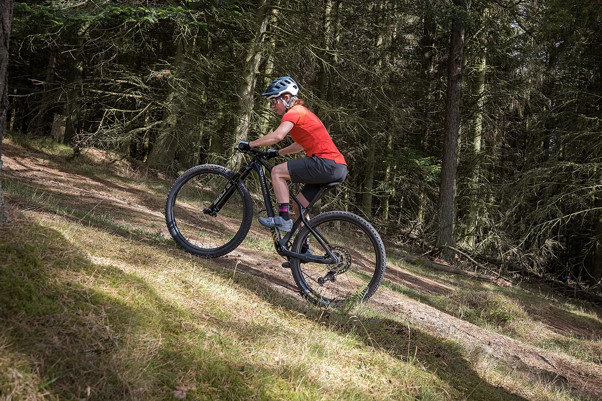 Cyclist in red top riding the Decathlon Rockrider MTB Race 900 Team Edition hardtail through woodland