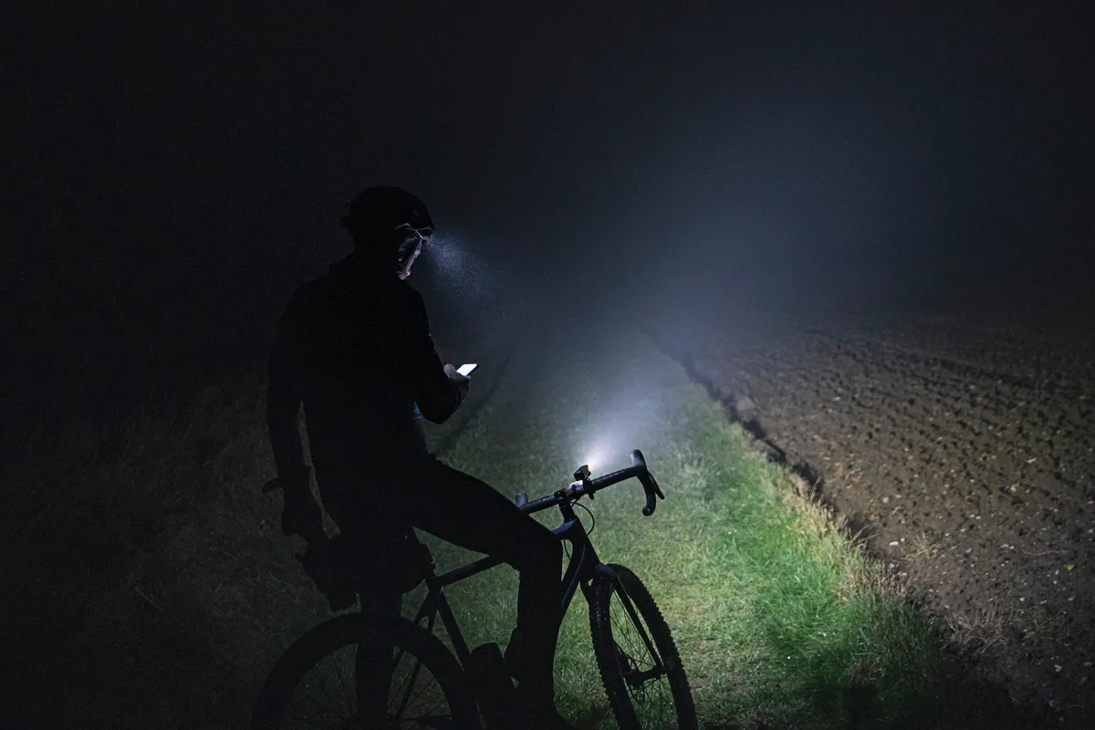Cyclist checking for directions on smartphone whilst out in the countryside on a dark foggy evening